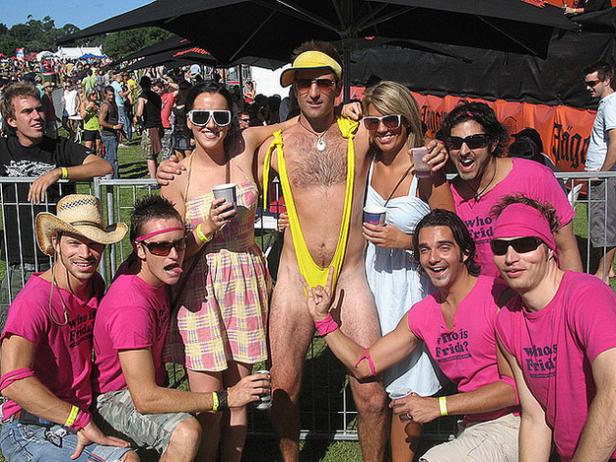 Eine Gruppe von Menschen posiert auf einem Festival, ein Mann trägt einen gelben String-Badeanzug.