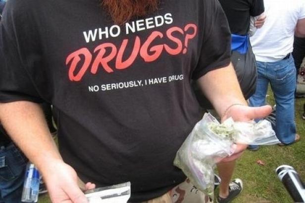 Ein Mann mit einem T-Shirt mit der Aufschrift „Who needs drugs? No seriously, I have drugs“ hält eine Tüte mit Marihuana.