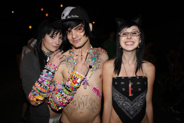 Drei junge Leute posieren mit bunten Armbändern und auffälligem Make-up für ein Foto.