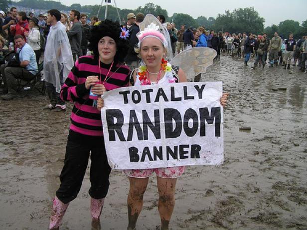 Zwei Frauen stehen im Schlamm und halten ein Schild mit der Aufschrift „Totally Random Banner“.