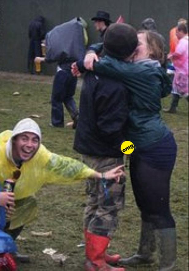 Ein Paar küsst sich auf einem Festival, während ein Mann im gelben Regenmantel in die Kamera grinst.