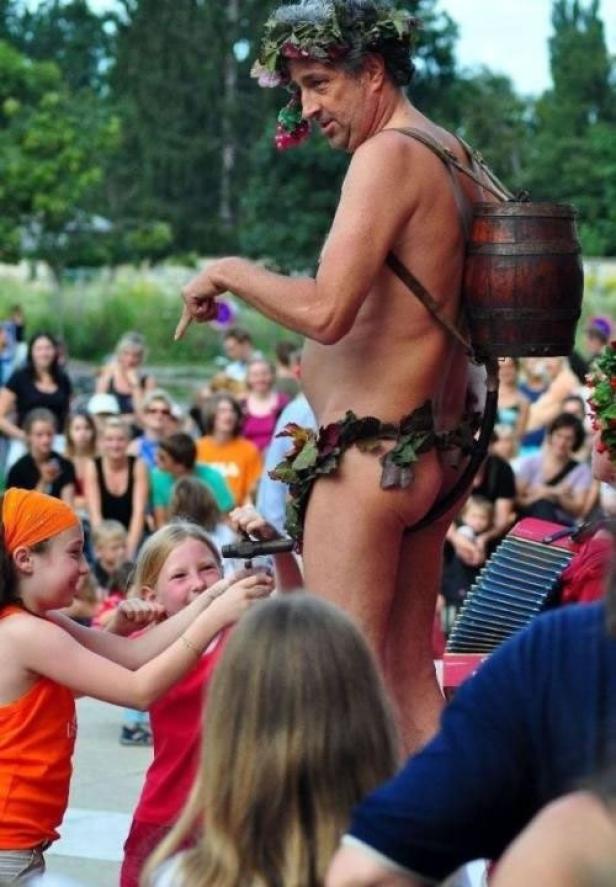 Ein Mann, als römischer Gott verkleidet, steht vor einer Menschenmenge.