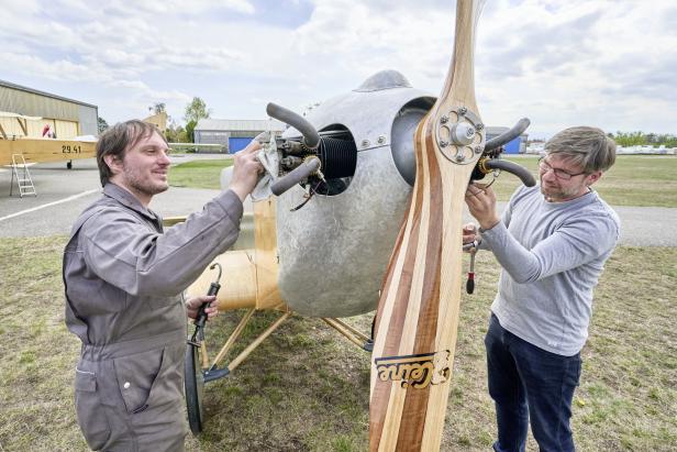 Zwei Männer arbeiten an einem Oldtimer-Flugzeug mit einem hölzernen Propeller.