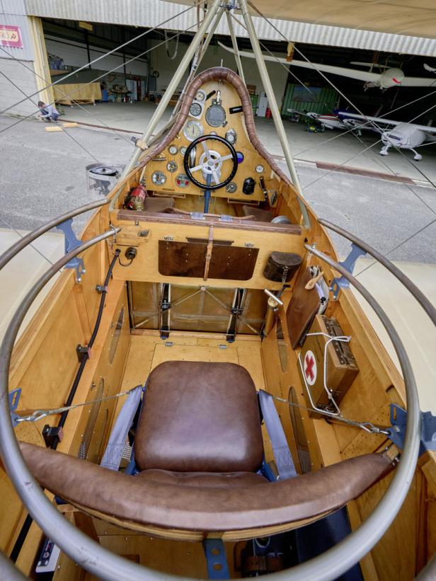 Das Cockpit eines historischen Flugzeugs mit Steuerrad, Instrumenten und einem braunen Ledersitz.
