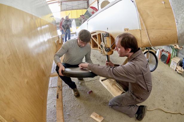 Zwei Männer arbeiten an der Restaurierung eines historischen Flugzeugs in einer Werkstatt.