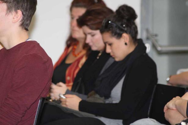 Mehrere Personen sitzen in einer Reihe und schauen auf ihre Handys.