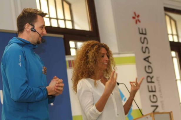 Eine Frau mit lockigem Haar hält eine Präsentation, während ein Mann mit Headset daneben steht.