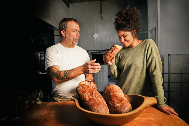 Ein Bäcker und eine Frau betrachten und riechen ein frisch gebackenes Brot.