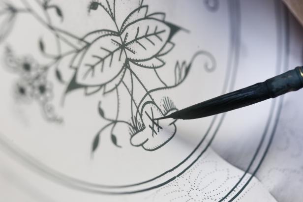 Eine Person zeichnet mit einer Feder und Tinte ein florales Muster auf Papier.