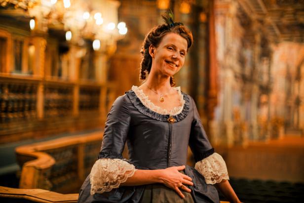 Eine Frau in historischer Kleidung lächelt in einem Theater.