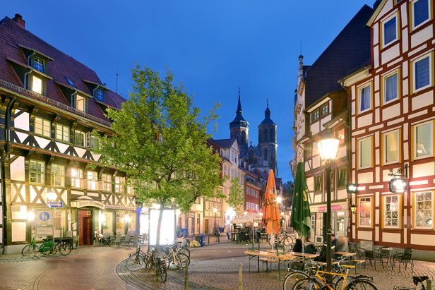 Eine abendliche Szene in einer deutschen Stadt mit Fachwerkhäusern und einer Kirche im Hintergrund.