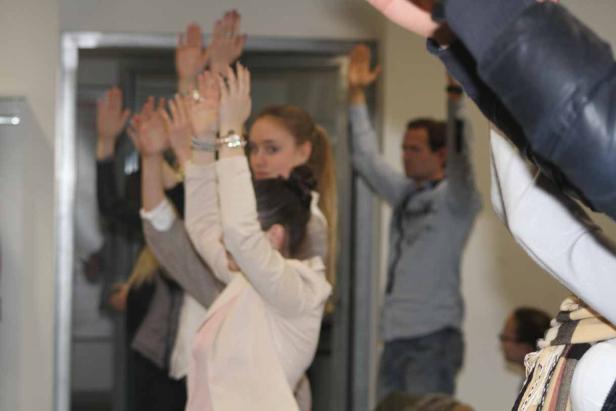 Eine Gruppe von Menschen steht mit erhobenen Händen in einem Raum.