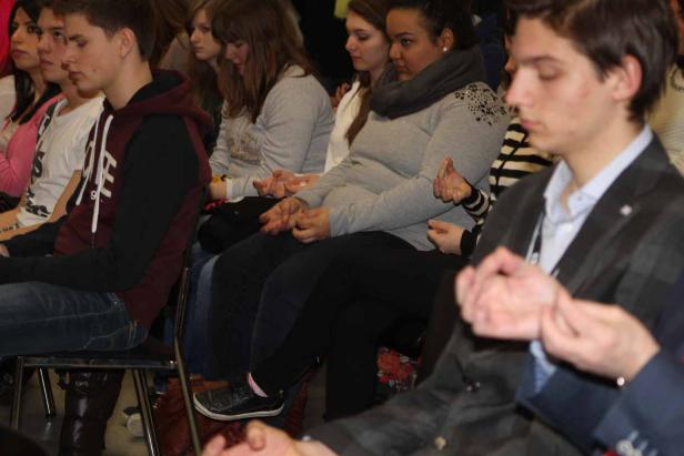 Eine Gruppe junger Leute sitzt auf Stühlen und hält die Hände in einer bestimmten Position.