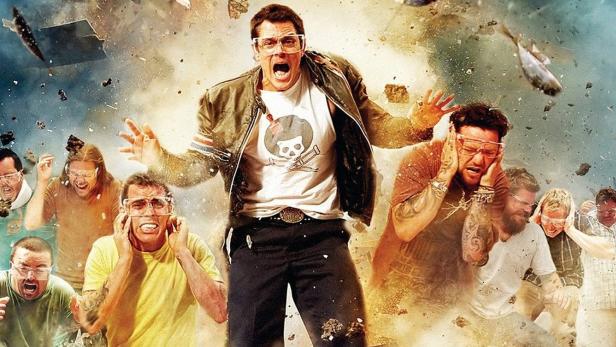 Eine Gruppe von Männern, darunter Johnny Knoxville, schreit inmitten einer Explosion und umherfliegender Gegenstände.