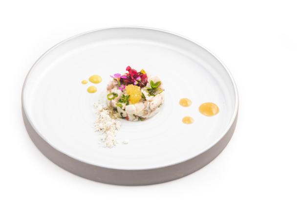 Ein Teller mit einem kunstvoll angerichteten Fisch-Tartar, garniert mit Blüten und einer hellen Sauce.