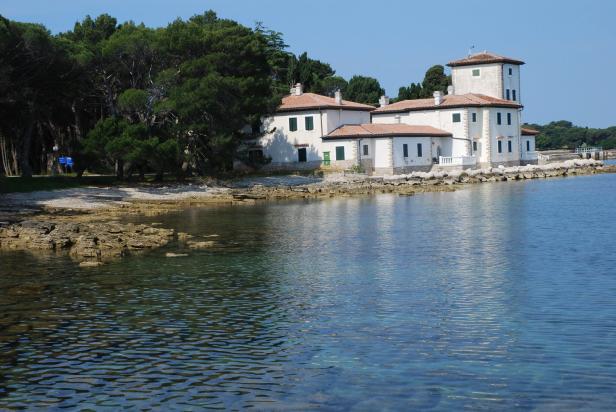 Ein weißes Gebäude mit einem Turm steht an einer felsigen Küste am Meer.