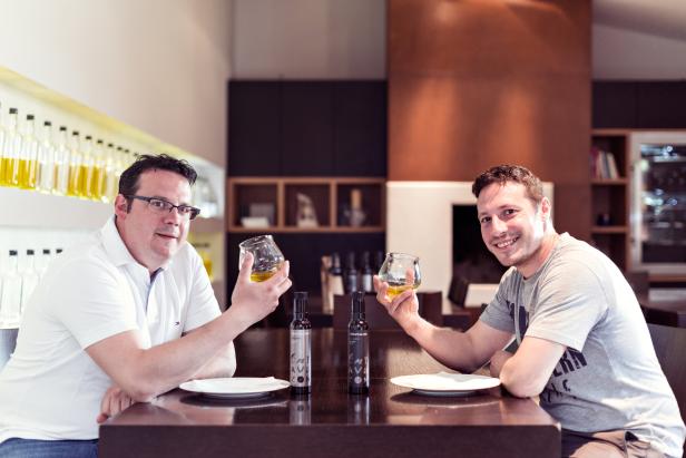 Zwei Männer sitzen an einem Tisch und probieren Olivenöl.