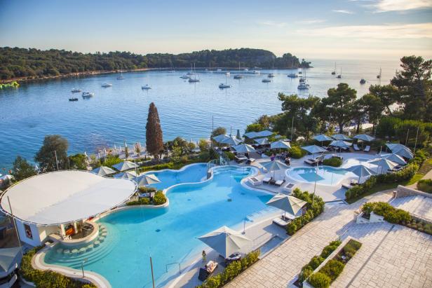 Blick auf einen Hotelpool mit Meerblick und zahlreichen Segelbooten.