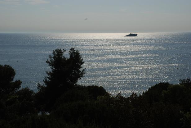 Blick auf das glitzernde Meer mit einer kleinen Insel am Horizont.