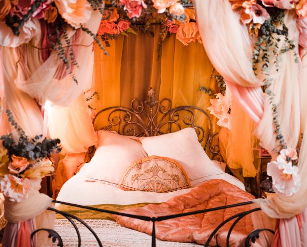 Ein Himmelbett mit Blumen und drapierten Stoffen in warmen Farbtönen.