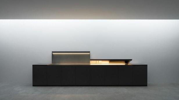 Ein schwarzer Küchenschrank mit integrierter Beleuchtung vor einer weißen Wand.