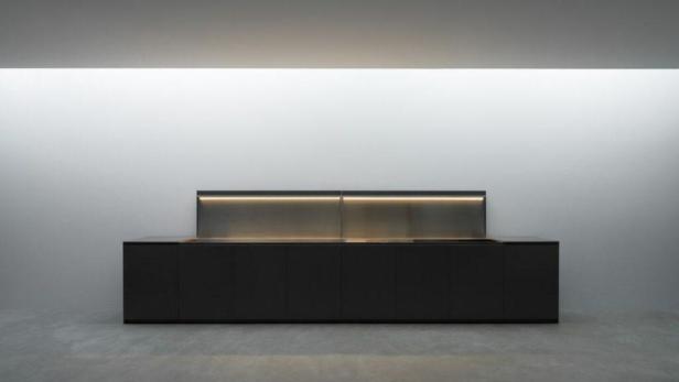 Eine moderne, schwarze Küchenzeile mit indirekter Beleuchtung vor einer weißen Wand.