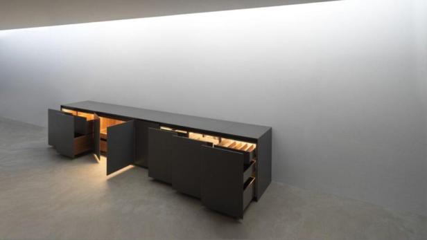 Ein langer, dunkler Schrank mit offenen Türen und Schubladen steht in einem Raum.