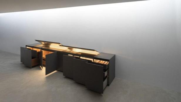 Ein moderner, schwarzer Schrank mit offenen Türen und Schubladen steht in einem hellen Raum.