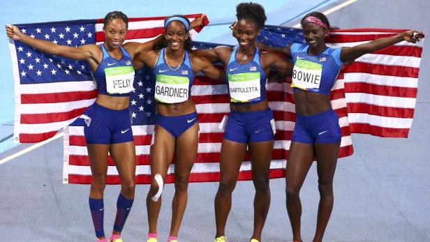 Das US-amerikanische 4x100-Meter-Staffelteam der Frauen feiert mit der US-Flagge.