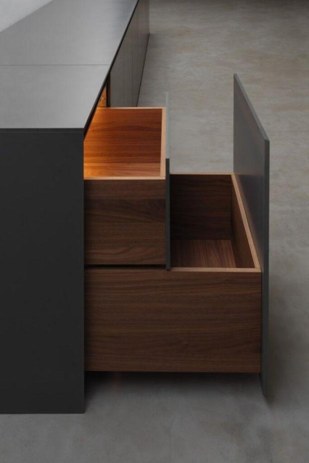 Ein grauer Küchenschrank mit zwei offenen Holzschubladen.