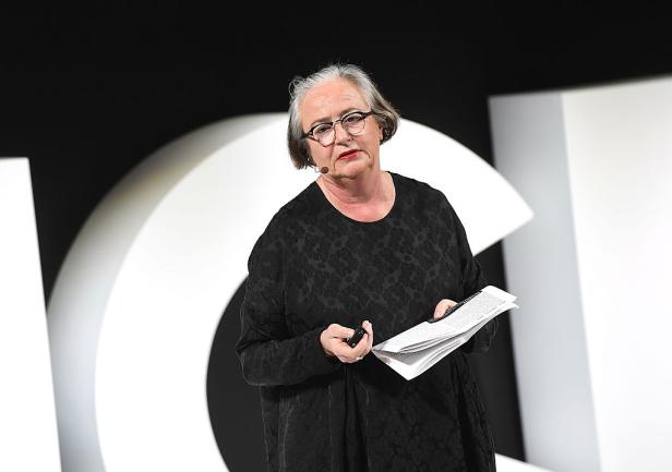 Eine Frau mit Brille hält ein Manuskript in der Hand und spricht.