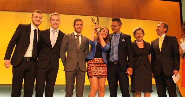 Eine Gruppe von Menschen posiert mit einer Trophäe vor einem gelben Hintergrund der Österreichischen Lotterien.