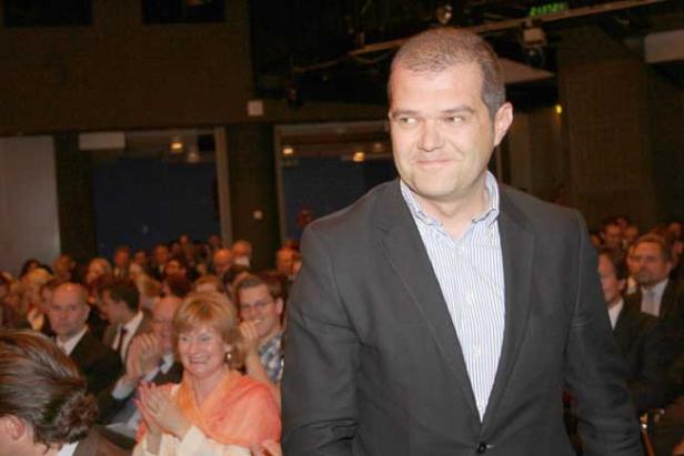 Ein Mann in einem Anzug steht vor einem applaudierenden Publikum.