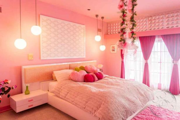 Ein rosa Schlafzimmer mit einem Bett, Herzförmigen Kissen und Blumenverzierungen.