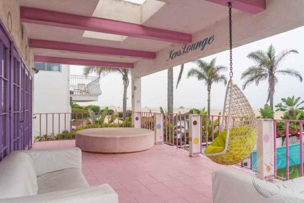 Eine Terrasse im Retro-Stil mit rosa Boden, Palmen und einer Hängematte.