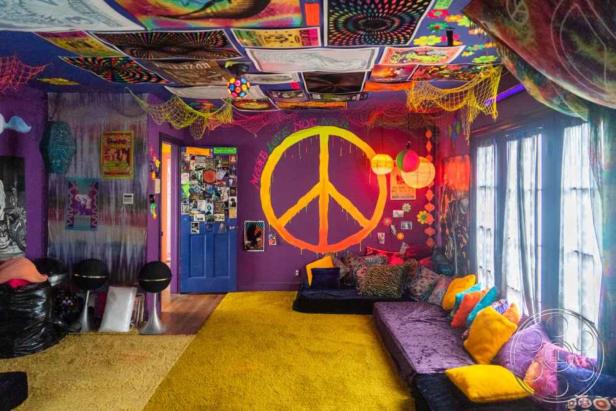 Ein Zimmer im Hippie-Stil mit einem großen Peace-Zeichen an der Wand und psychedelischen Postern an der Decke.