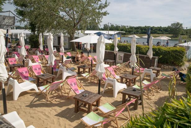 Viele Liegestühle und Tische stehen auf einem Sandstrand bereit.