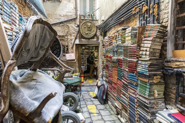 Ein schmaler venezianischer Durchgang mit einem Bücherladen und gestapelten Büchern an den Wänden.