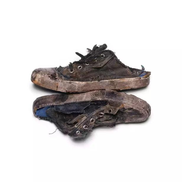 Zwei extrem abgenutzte und beschädigte Turnschuhe liegen übereinander.