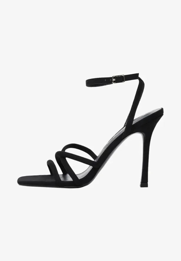 Ein schwarzer, hochhackiger Riemchensandalen vor einem weißen Hintergrund.