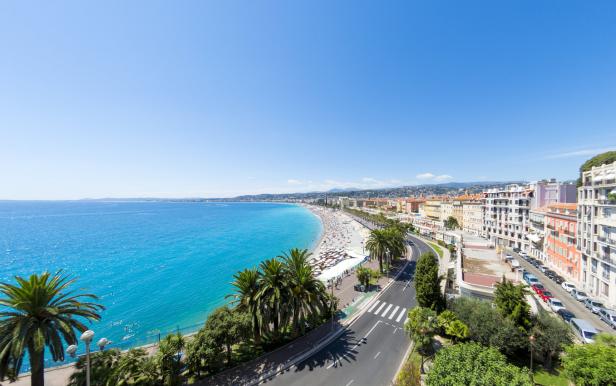 Ein Panoramablick auf die Küste von Nizza mit Strand, Palmen und Gebäuden.