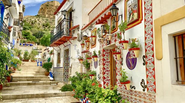 Eine malerische Gasse in einer spanischen Stadt mit blühenden Pflanzen und dekorativen Fassaden.