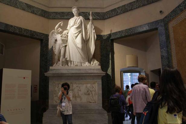 Eine Statue der Göttin Venus mit Amor in einem Museum, umgeben von Besuchern.