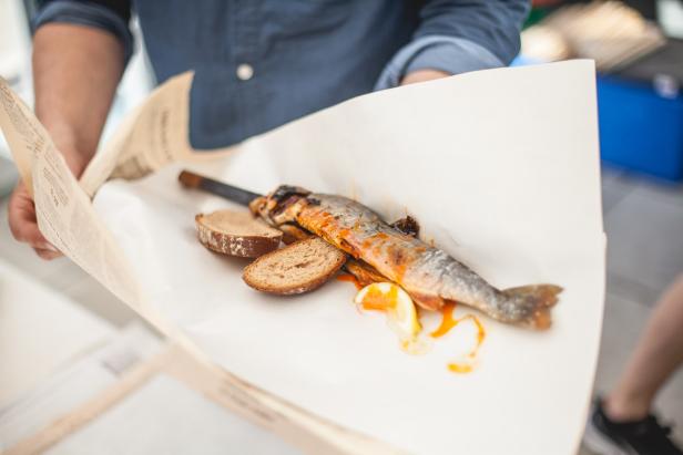 Ein gegrillter Fisch mit Brot und Zitrone wird auf Papier serviert.