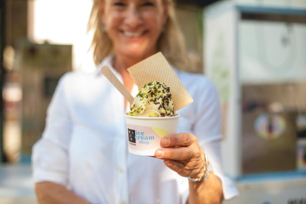 Eine Frau hält einen Eisbecher mit Waffel und Streuseln in der Hand.