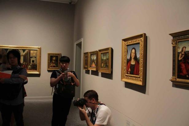 Besucher betrachten und fotografieren Gemälde in einem Kunstmuseum.