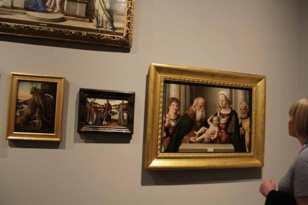 Eine Frau betrachtet ein Gemälde der Madonna mit Kind und Heiligen in einem goldenen Rahmen.