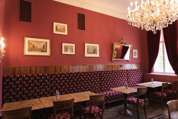 Innenansicht eines traditionellen Wiener Kaffeehauses mit roter Wand und Kristalllüster.