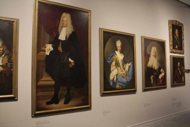 Mehrere gerahmte Porträtgemälde hängen an einer Wand in einer Kunstgalerie.