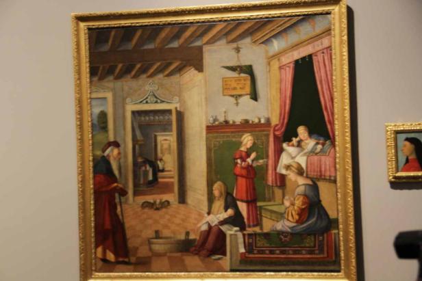 Das Gemälde zeigt eine häusliche Szene mit mehreren Frauen und einem älteren Mann in einem Innenraum.